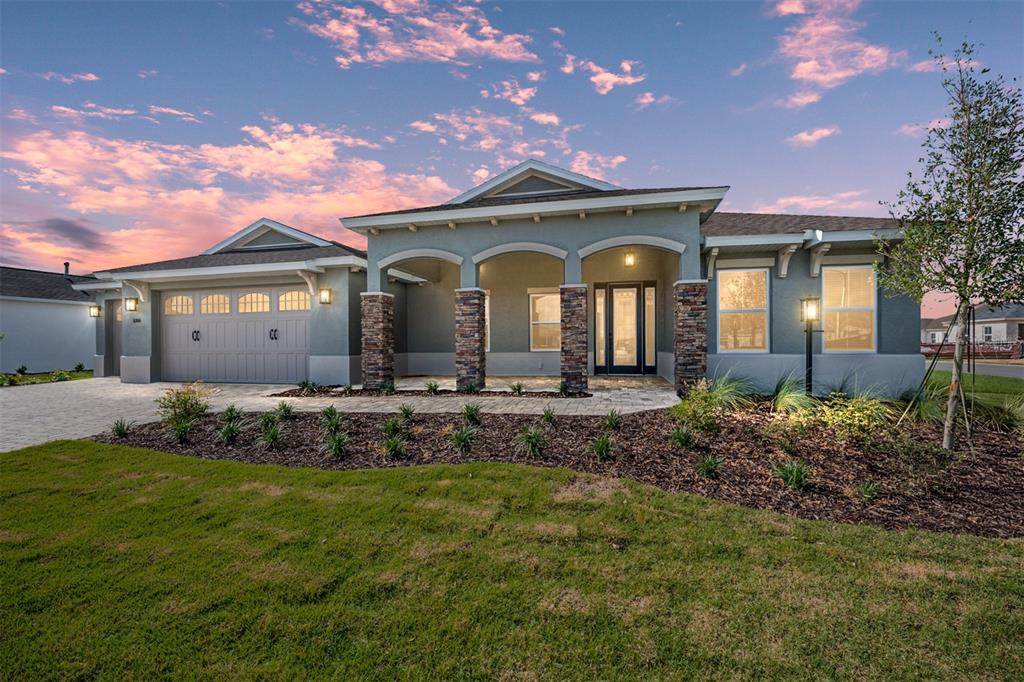 A single-story house with a gray stucco exterior, stone columns, and a paved driveway at sunset — 10306 SW 85TH PLACE ROAD, OCALA, FL