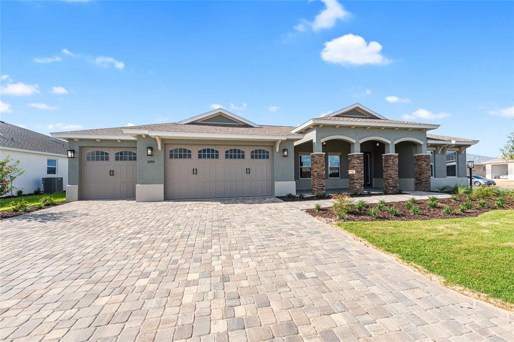A single-story house with a stone-accented porch, a three-car garage, and a paver driveway — 10306 SW 85TH PLACE ROAD, OCALA, FL
