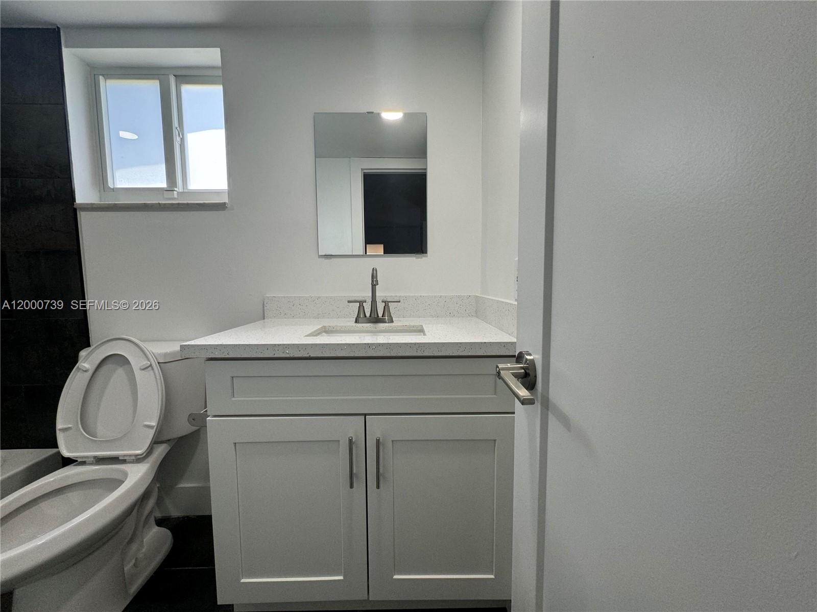A bathroom features a white vanity with a speckled countertop, a mirror, and a toilet — 4850 SW 26th Ave # 6, Dania Beach FL 33312, DANIA BEACH, FL