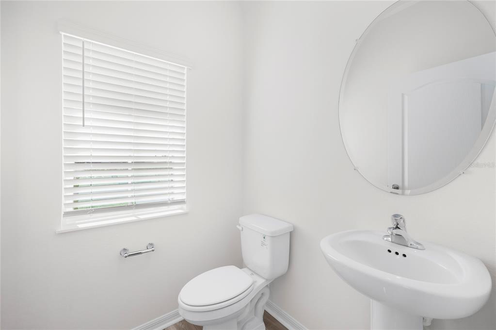 A bright half bathroom features a pedestal sink, round mirror, toilet, and white window blinds — 636 TANGELO TERRACE, BABSON PARK, FL
