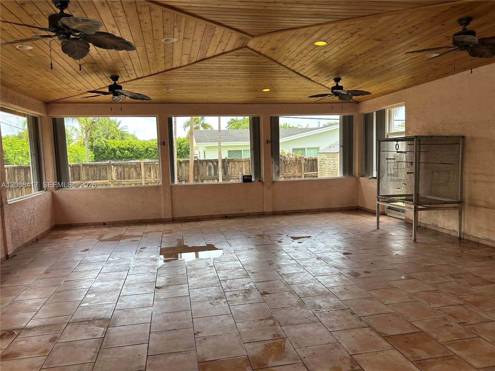 A covered patio features a wood-paneled ceiling, tile flooring, and large windows overlooking a yard — 8385 SW 105th St, Miami FL 33156, MIAMI, FL