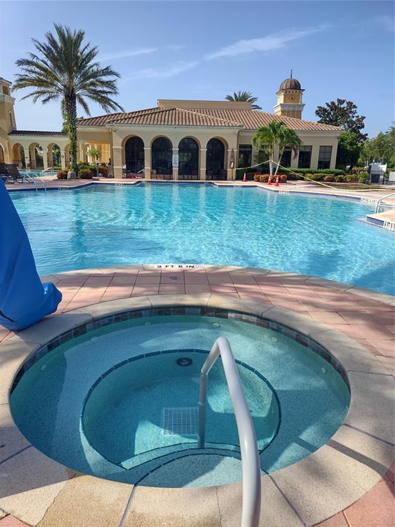 A circular hot tub sits in the foreground with a large swimming pool and clubhouse behind — 150 PADOVA WAY UNIT 43, NOKOMIS, FL