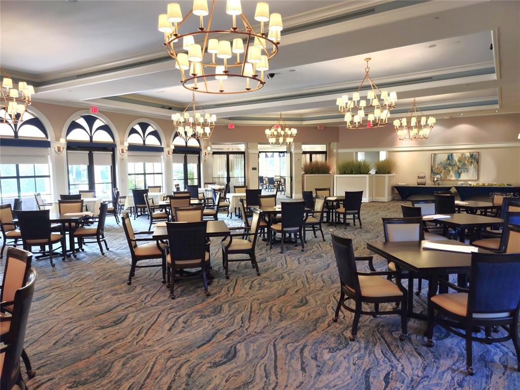 A spacious dining room features multiple chandeliers, dark wooden tables, and patterned blue carpeting — 150 PADOVA WAY UNIT 43, NOKOMIS, FL