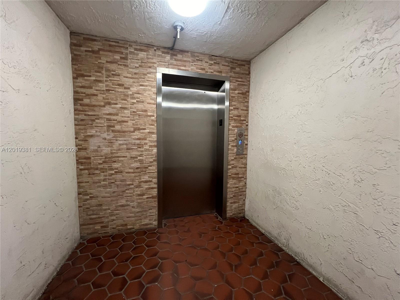 An elevator with a stainless steel door is set against a textured stone accent wall — 9431 SW 4th St # 207, Miami FL 33174, MIAMI, FL