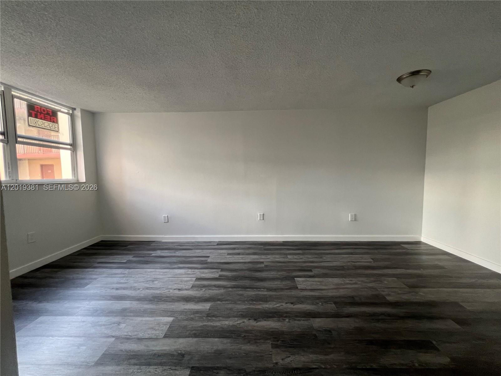 An empty room features gray wood-look flooring, white walls, and a single window — 9431 SW 4th St # 207, Miami FL 33174, MIAMI, FL