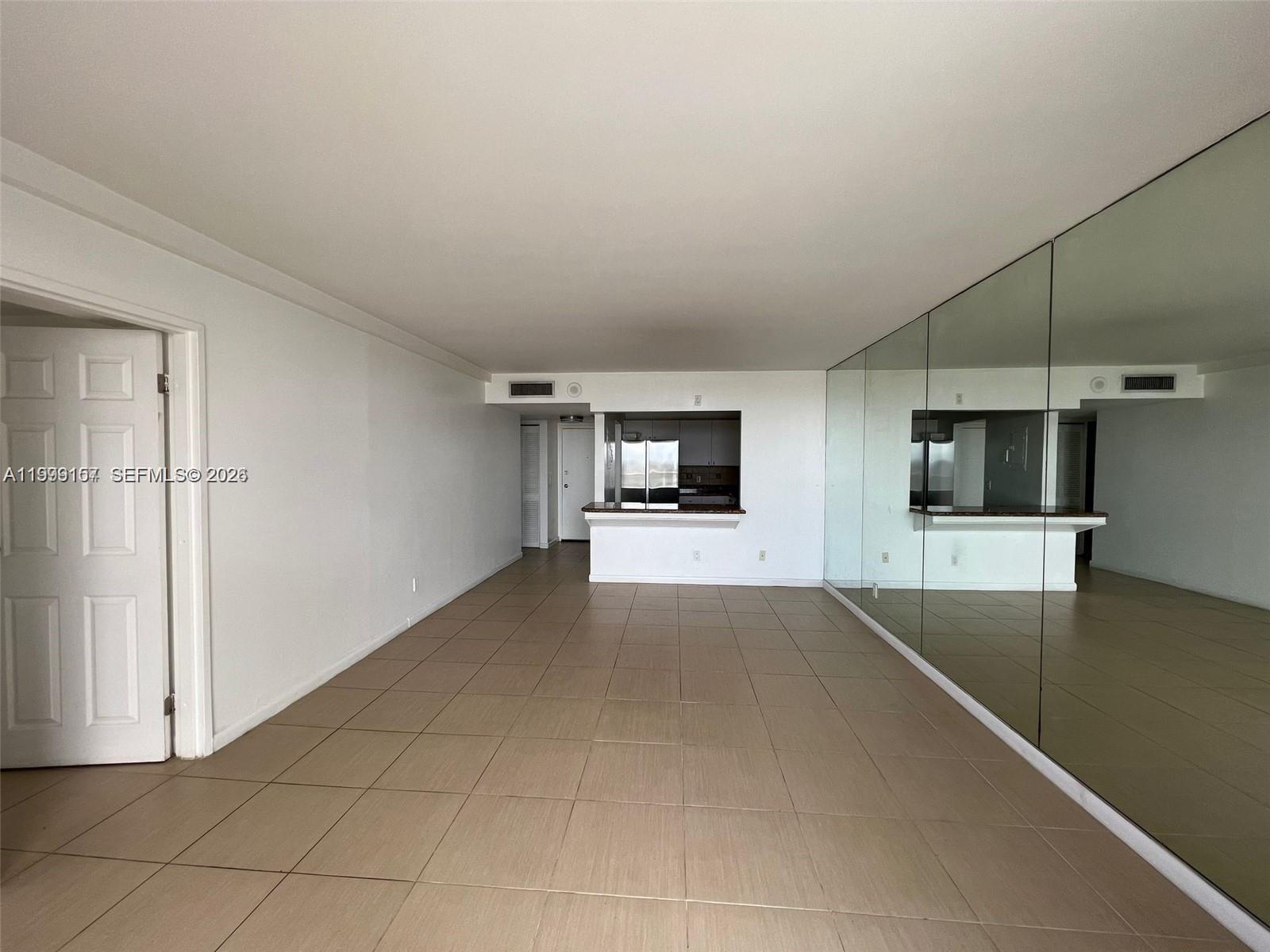 An empty room features beige tile flooring, white walls, and a large mirrored accent wall — 13499 Biscayne Blvd # 1402, North Miami FL 33181, NORTH MIAMI, FL