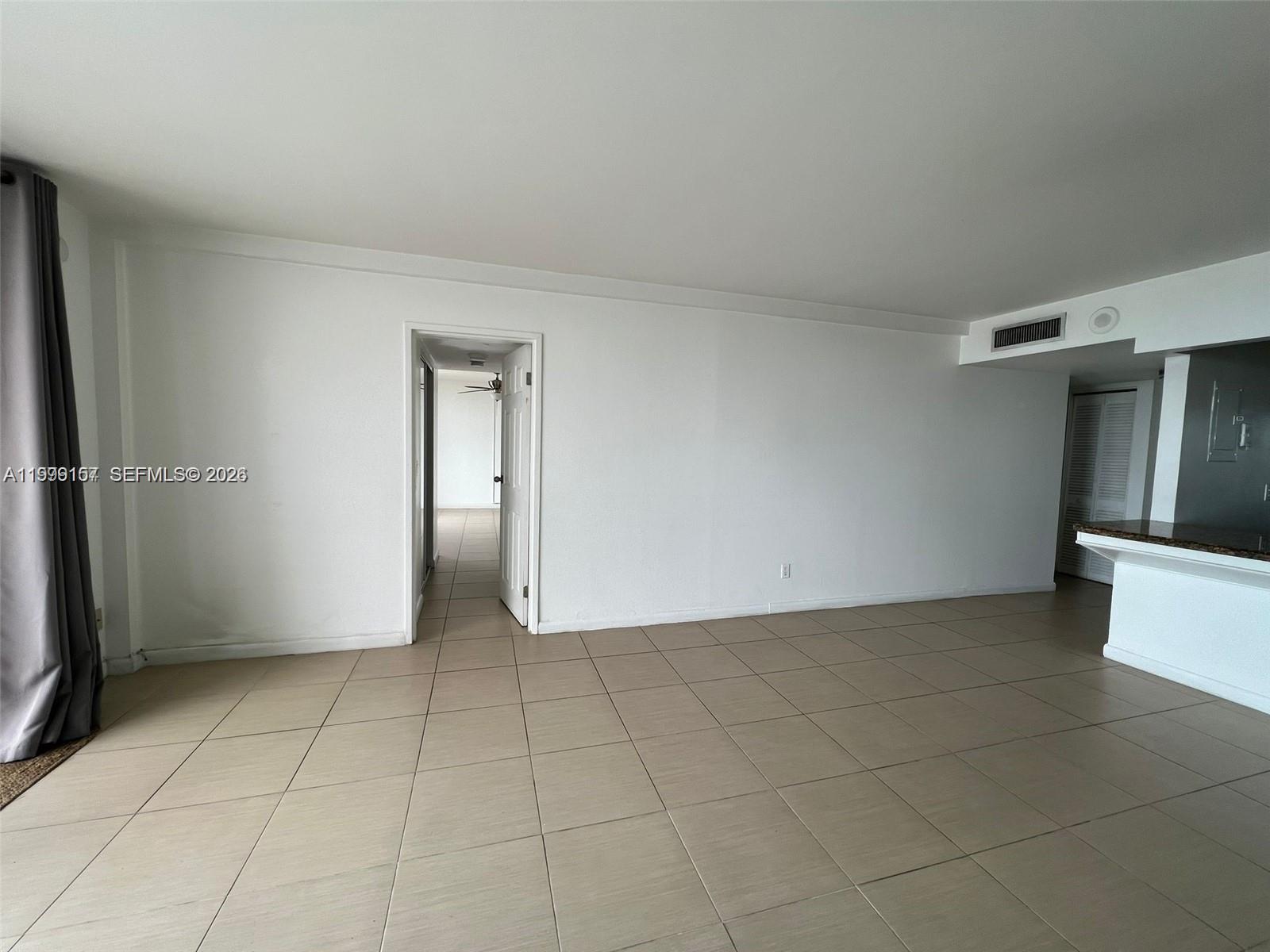 An empty room with beige tile flooring, white walls, and a doorway leading to another room — 13499 Biscayne Blvd # 1402, North Miami FL 33181, NORTH MIAMI, FL