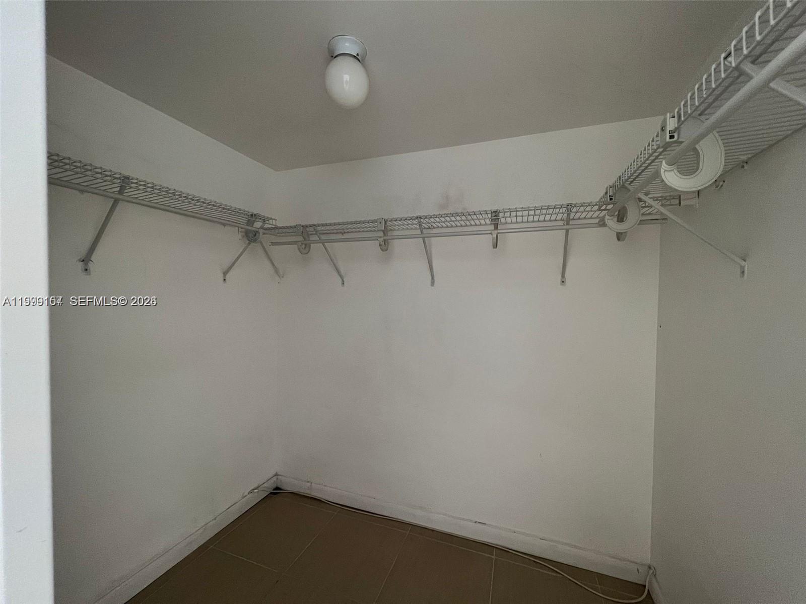 A walk-in closet features white walls, tile flooring, and wire shelving along the walls — 13499 Biscayne Blvd # 1402, North Miami FL 33181, NORTH MIAMI, FL