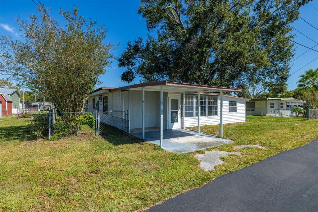 A single-story mobile home with a white exterior, a front carport, and a chain-link fence — 39019 HEATH DRIVE, ZEPHYRHILLS, FL
