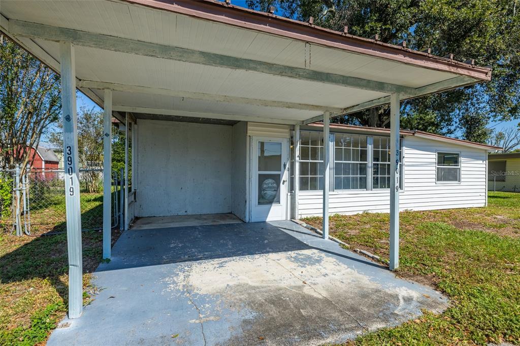 A white house features a covered carport with a concrete floor and a storm door — 39019 HEATH DRIVE, ZEPHYRHILLS, FL