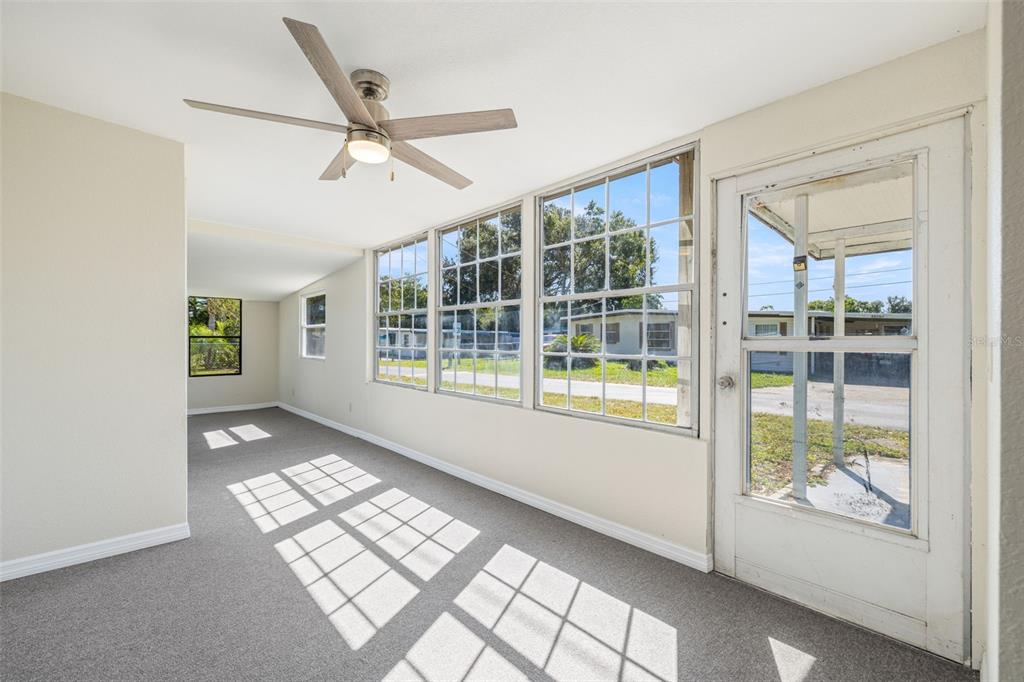 A sunroom with gray carpeting, a ceiling fan, large windows, and a white screen door — 39019 HEATH DRIVE, ZEPHYRHILLS, FL