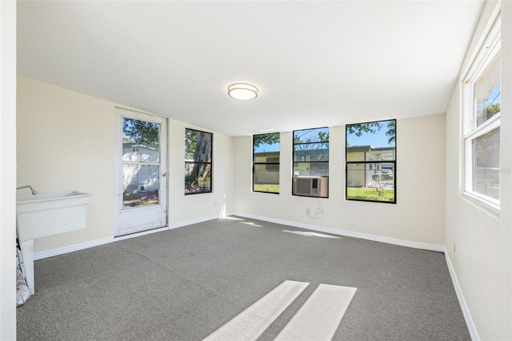 A sunroom with gray carpeting, a utility sink, and multiple windows looking out onto a yard — 39019 HEATH DRIVE, ZEPHYRHILLS, FL