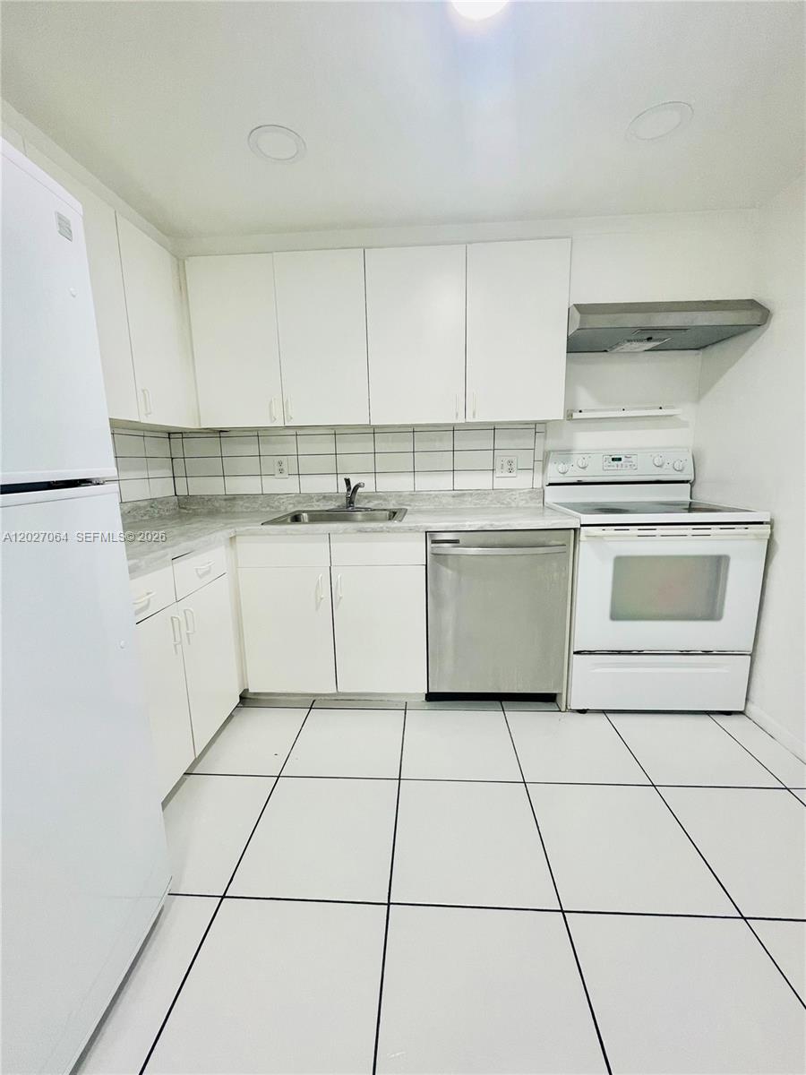 A kitchen features white cabinetry, a stainless steel dishwasher, a white stove, and tiled flooring — 13499 Biscayne Blvd # 1613, North Miami FL 33181, NORTH MIAMI, FL