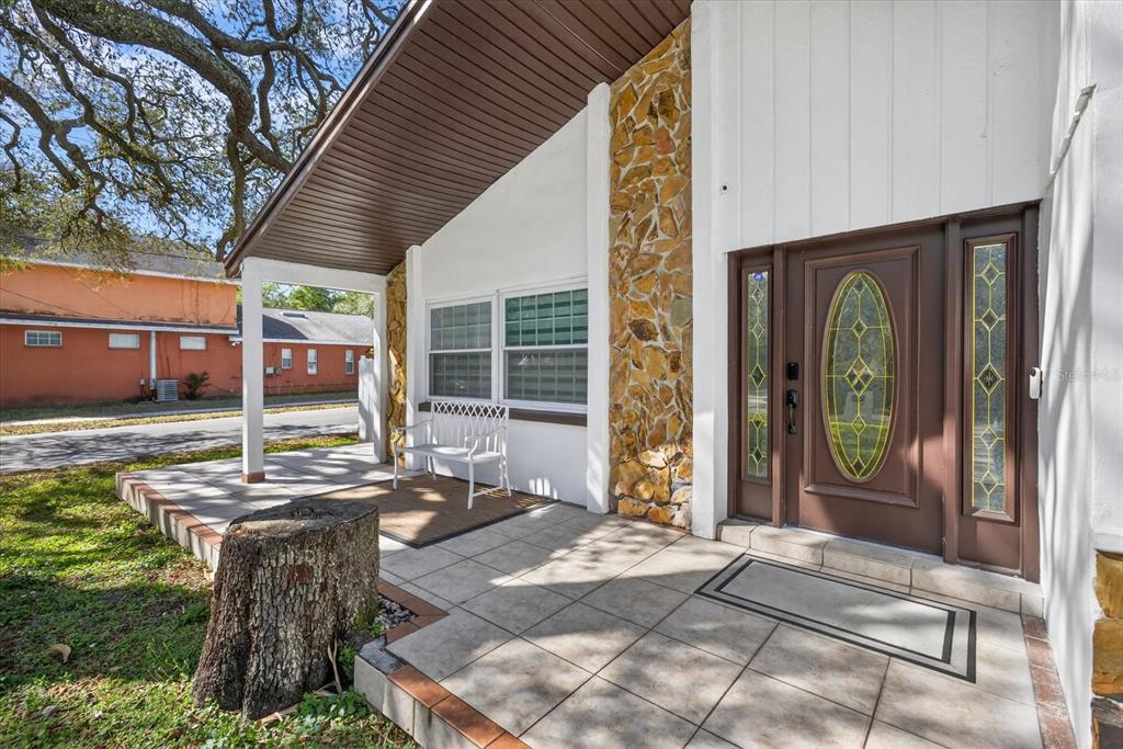 A front porch with a tiled floor, a white bench, and a stone-accented exterior wall — 8902 N HAMNER AVENUE, TAMPA, FL