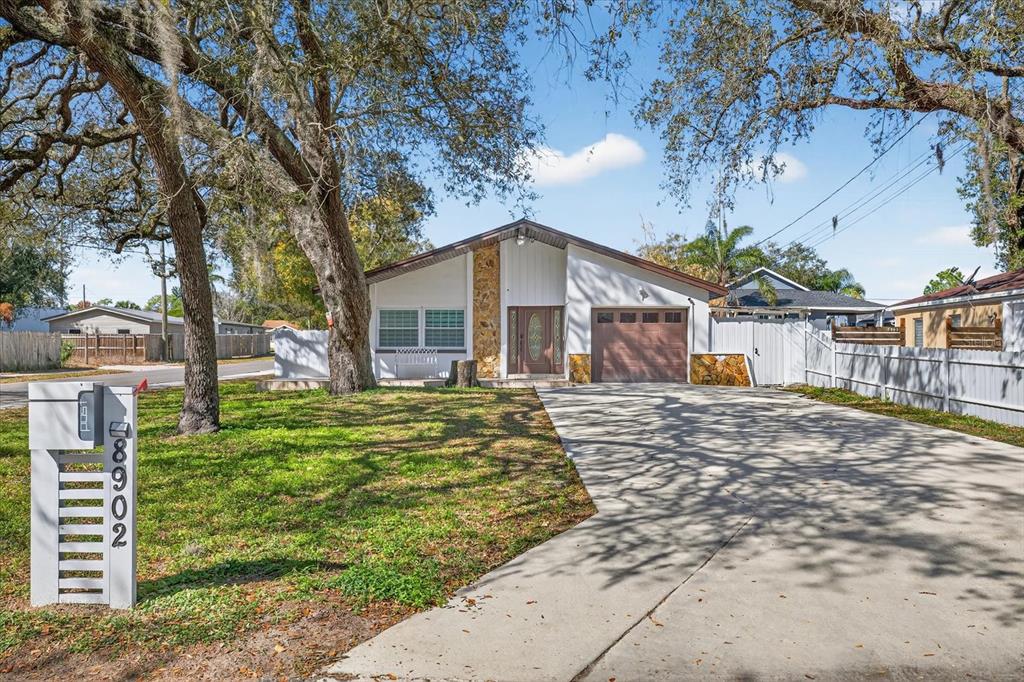 A single-story house with a concrete driveway, stone accents, and a large tree in front — 8902 N HAMNER AVENUE, TAMPA, FL