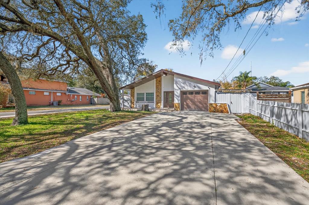 A single-story house with a concrete driveway, stone accents, and large oak trees in front — 8902 N HAMNER AVENUE, TAMPA, FL