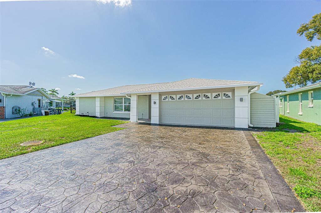 A single-story house features a stamped concrete driveway, a two-car garage, and light-colored siding — 1125 FERNWOOD DRIVE, HOLIDAY, FL