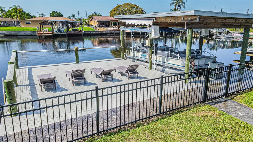 A fenced wooden dock features four lounge chairs and a covered boat slip on water — 1125 FERNWOOD DRIVE, HOLIDAY, FL