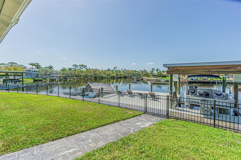 A grassy backyard features a stone walkway, a black metal fence, and a boat dock — 1125 FERNWOOD DRIVE, HOLIDAY, FL