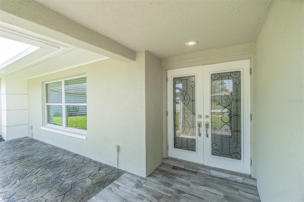 A covered entryway features a stone-patterned floor, a tiled porch, and double glass-paneled doors — 1125 FERNWOOD DRIVE, HOLIDAY, FL