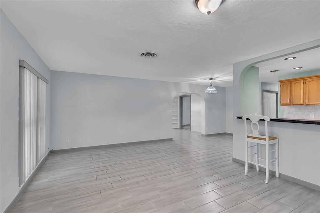 A living room with light gray tile flooring, white walls, and an arched kitchen pass-through — 3303 FLORIDA BOULEVARD, BRADENTON, FL