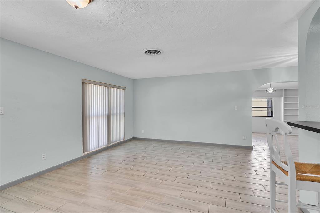 An empty living room features light-colored tile flooring, pale blue walls, and vertical window blinds — 3303 FLORIDA BOULEVARD, BRADENTON, FL