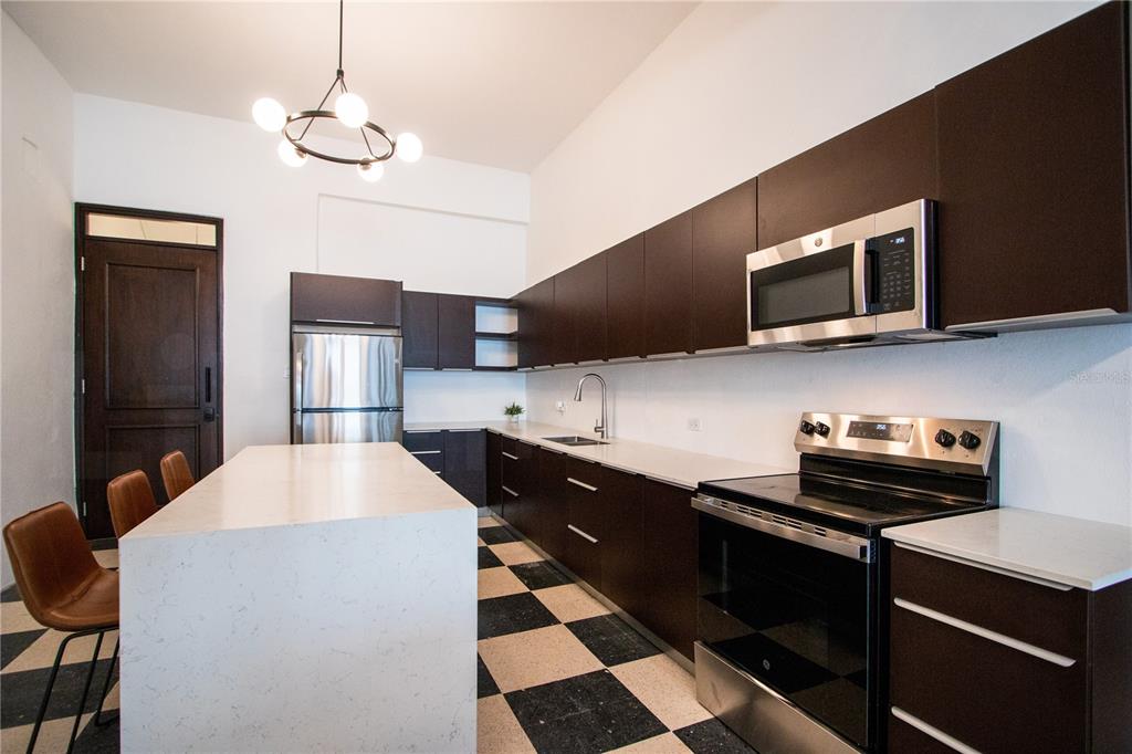 A modern kitchen features dark cabinetry, stainless steel appliances, a white island, and checkered flooring — 254-256 SAN FRANCISCO STREET UNIT 204, SAN JUAN, PR