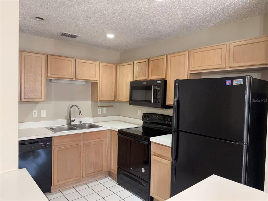 A kitchen features light wood cabinets, black appliances, a double-basin sink, and white tile flooring — 1206 N FAIRWAY DRIVE UNIT 1206, APOPKA, FL
