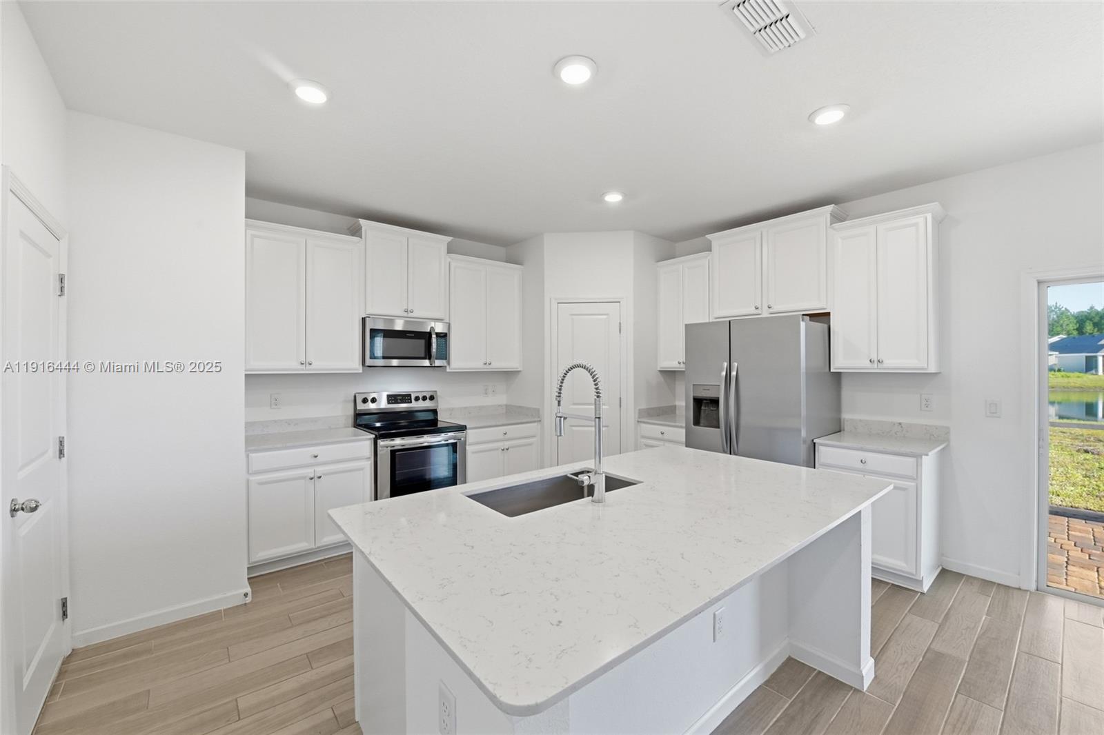 A modern kitchen features white cabinets, stainless steel appliances, and a large quartz-topped island — 9852 Lemon Balm Way, Jacksonville FL 32219, JACKSONVILLE, FL