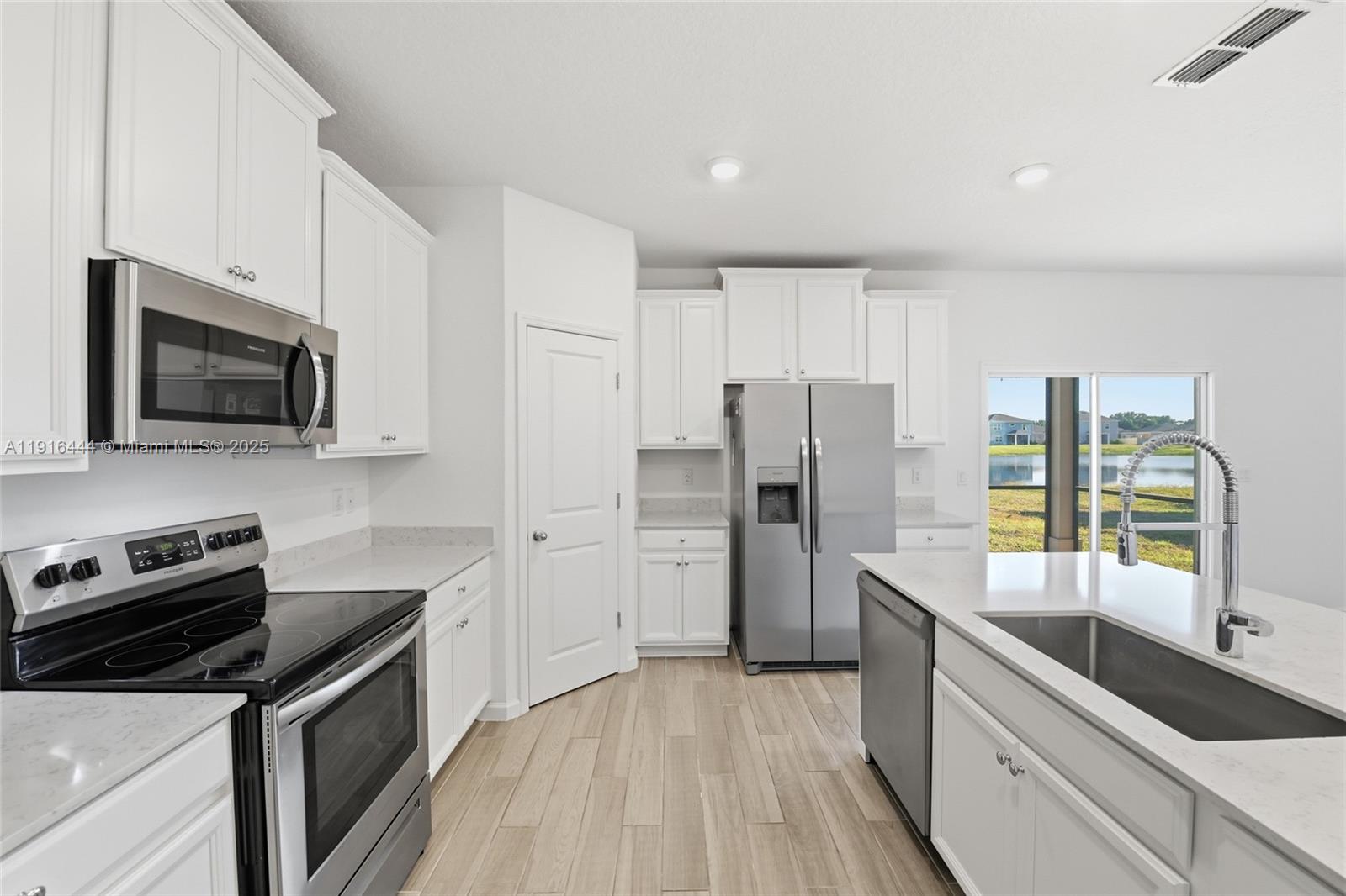 A modern kitchen features white cabinets, stainless steel appliances, quartz countertops, and a center island — 9852 Lemon Balm Way, Jacksonville FL 32219, JACKSONVILLE, FL