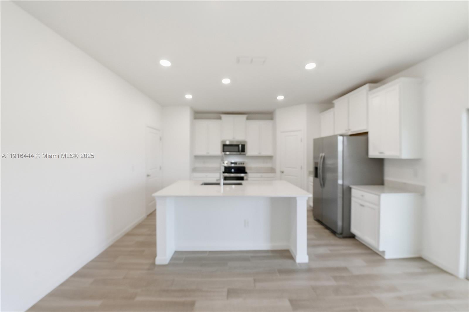 A modern kitchen features white cabinetry, a central island, and stainless steel appliances — 9852 Lemon Balm Way, Jacksonville FL 32219, JACKSONVILLE, FL