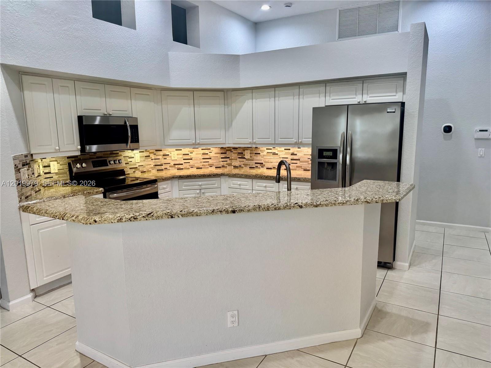 A kitchen features white cabinets, granite countertops, stainless steel appliances, and a breakfast bar — 2525 Bay Pointe Ct, Weston FL 33327, WESTON, FL