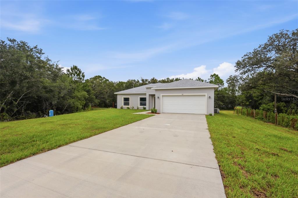 A single-story house with a white garage and concrete driveway sits on a grassy lot — 121 S CANOE CREEK ROAD, KENANSVILLE, FL