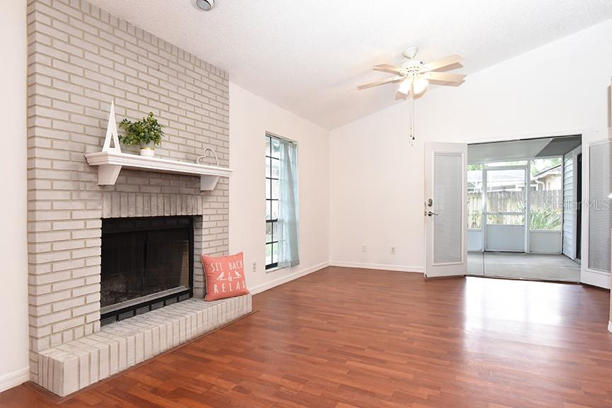A living room features a light brick fireplace, wood-look flooring, and a glass door entrance — 2213 PINE TREE DRIVE, EDGEWATER, FL