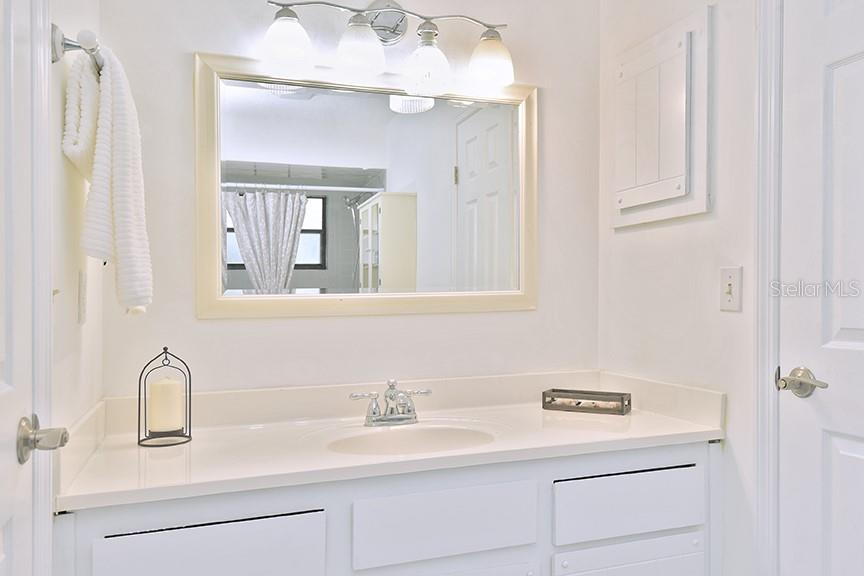 A bright bathroom features a white vanity, a framed mirror, and a wall-mounted light fixture — 2213 PINE TREE DRIVE, EDGEWATER, FL