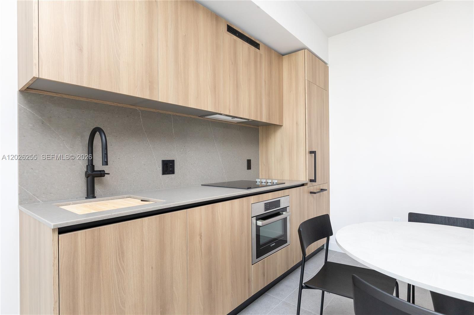 A modern kitchen features light wood cabinets, a gray stone backsplash, and black fixtures — 121 NE 5th St # 510, Miami FL 33132, MIAMI, FL