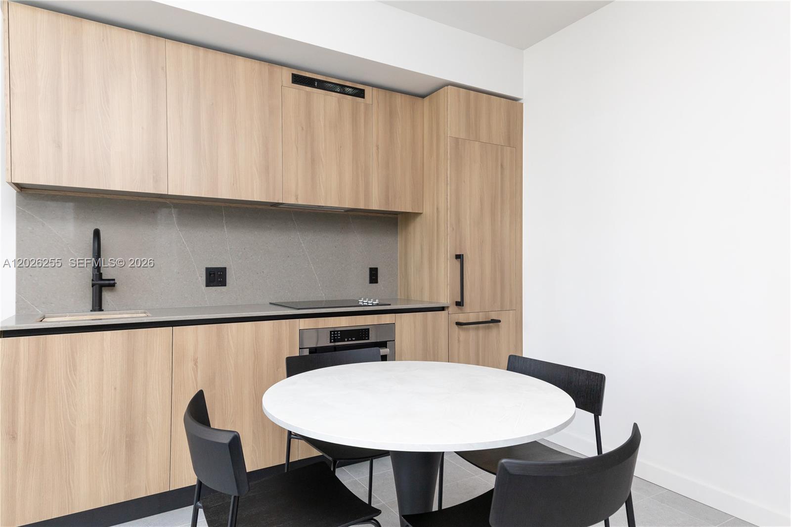 A modern kitchen features light wood cabinets, a grey stone backsplash, and a round dining table — 121 NE 5th St # 510, Miami FL 33132, MIAMI, FL