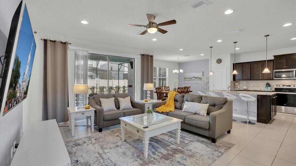 An open-concept living room and kitchen featuring gray sofas, a coffee table, and dark cabinetry — 2462 DUBAI STREET, KISSIMMEE, FL