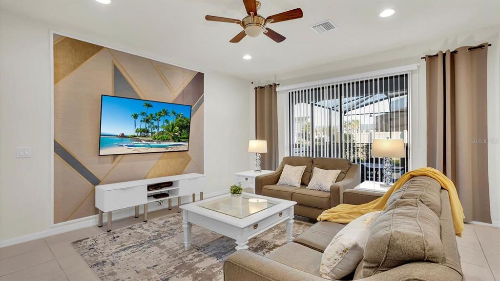 A living room features a geometric accent wall, a television, and neutral-toned furniture — 2462 DUBAI STREET, KISSIMMEE, FL