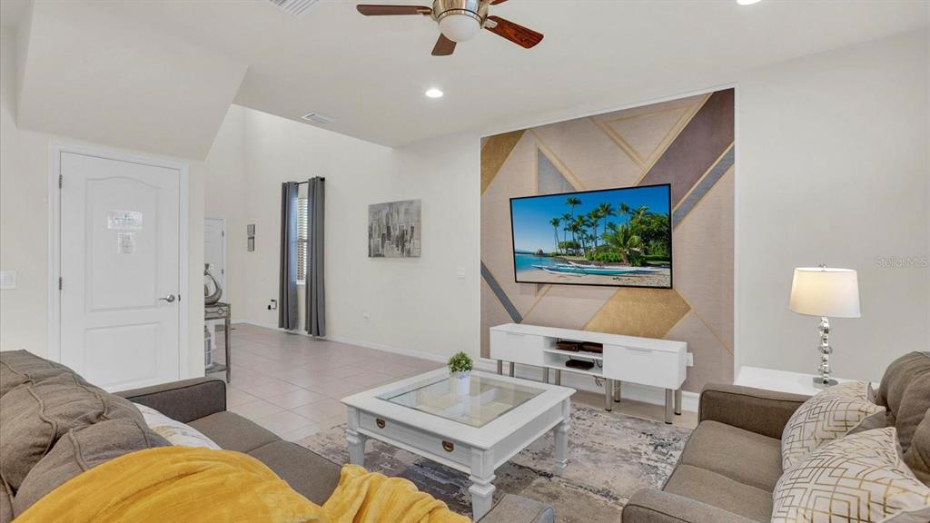 A living room features a geometric accent wall, a wall-mounted television, and a white coffee table — 2462 DUBAI STREET, KISSIMMEE, FL