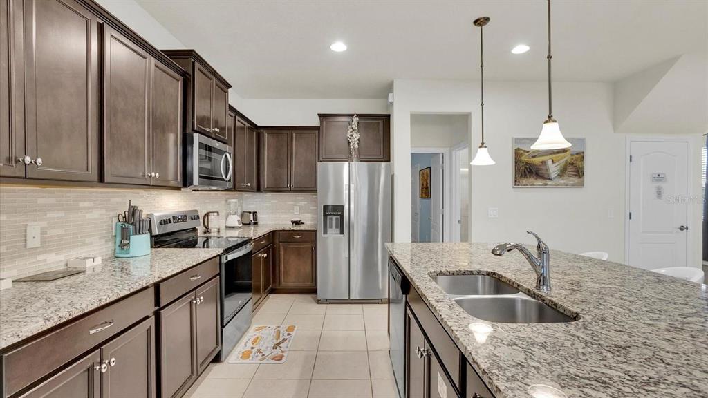 A kitchen featuring dark wood cabinets, granite countertops, stainless steel appliances, and a central island — 2462 DUBAI STREET, KISSIMMEE, FL