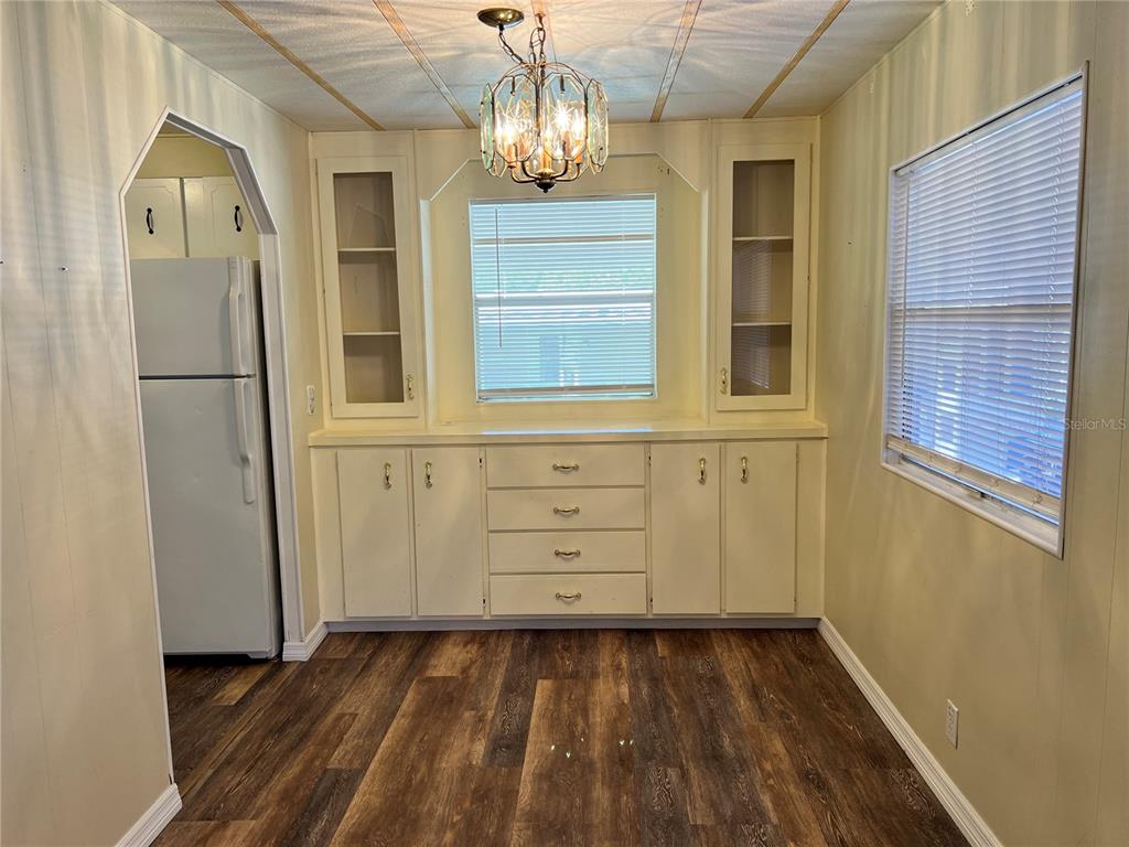 A dining area features built-in cabinetry, a chandelier, and wood-look flooring next to a refrigerator — 36 MAGNOLIA COURT UNIT 4, SAFETY HARBOR, FL