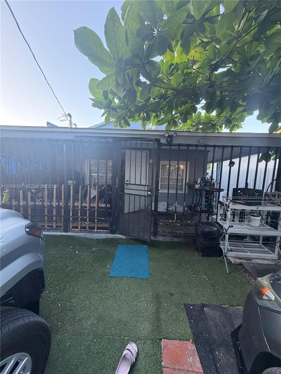 A small house exterior features a gated porch, artificial grass, and two parked vehicles — 1111 NW 26th St, Miami FL 33127, MIAMI, FL