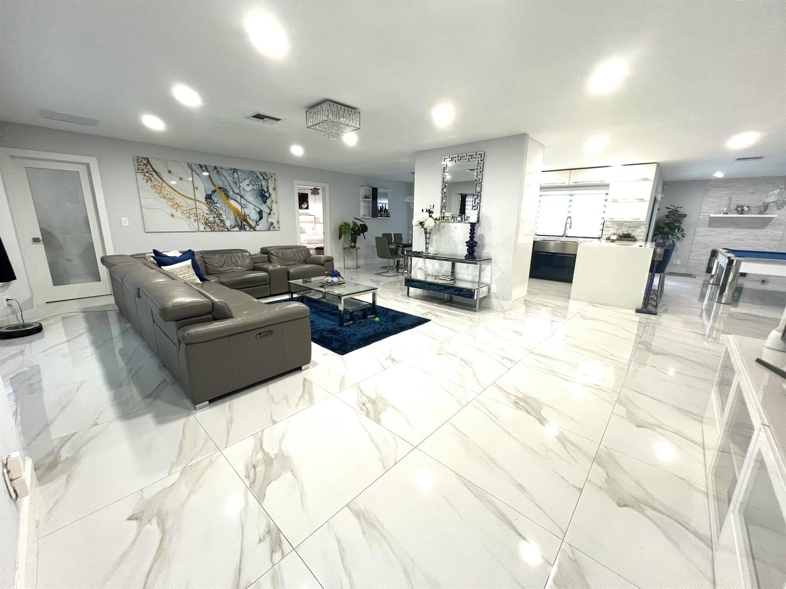 A spacious living room features large marble-look floor tiles, a grey sectional, and open kitchen — 625 W Tropical Way, Plantation FL 33317, PLANTATION, FL