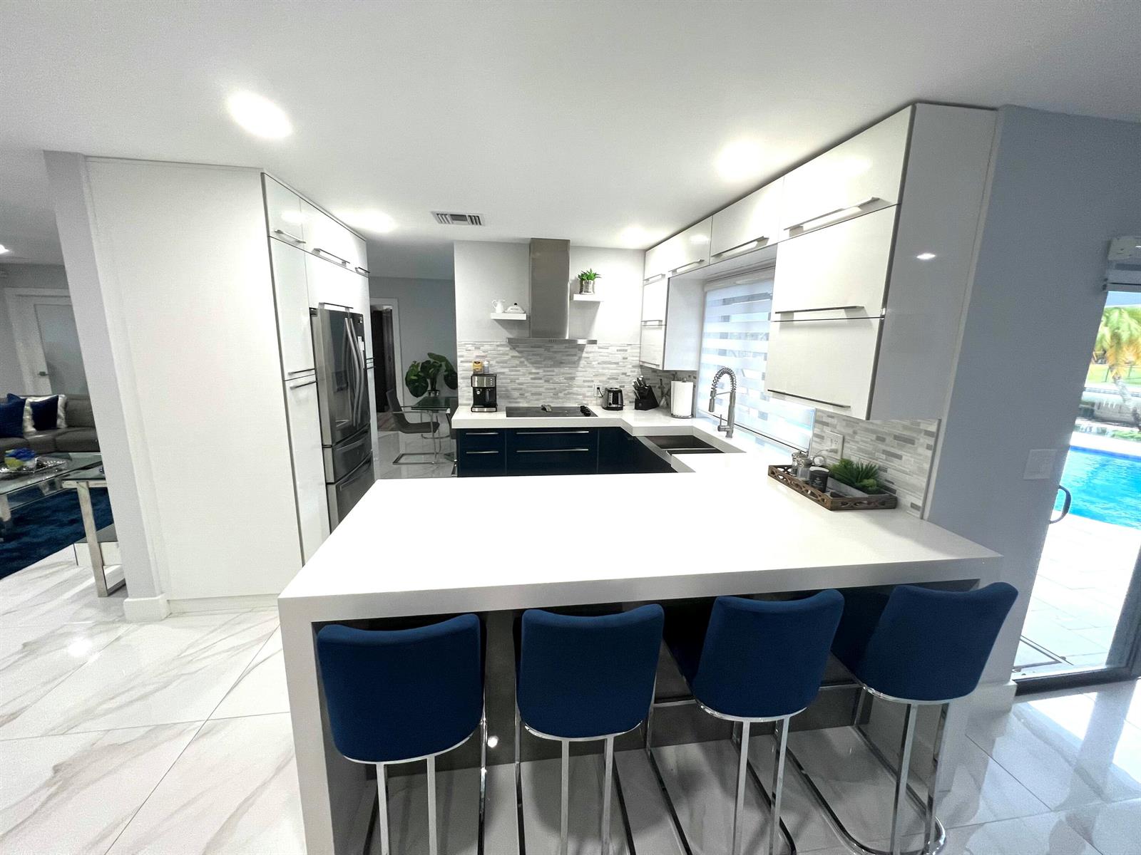 A modern kitchen features white cabinets, dark lower drawers, a breakfast bar, and blue stools — 625 W Tropical Way, Plantation FL 33317, PLANTATION, FL