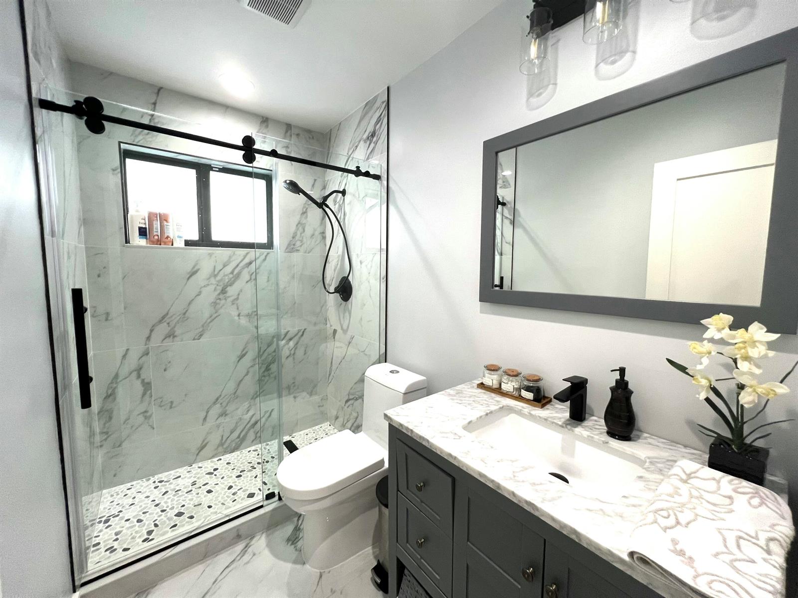 A modern bathroom features a marble-tiled walk-in shower, a gray vanity, and a matching mirror — 625 W Tropical Way, Plantation FL 33317, PLANTATION, FL
