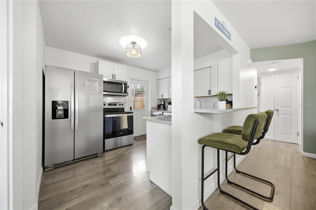 A kitchen features stainless steel appliances, white cabinetry, a breakfast bar, and wood-look flooring — 664 GRAY STREET S, ST PETERSBURG, FL