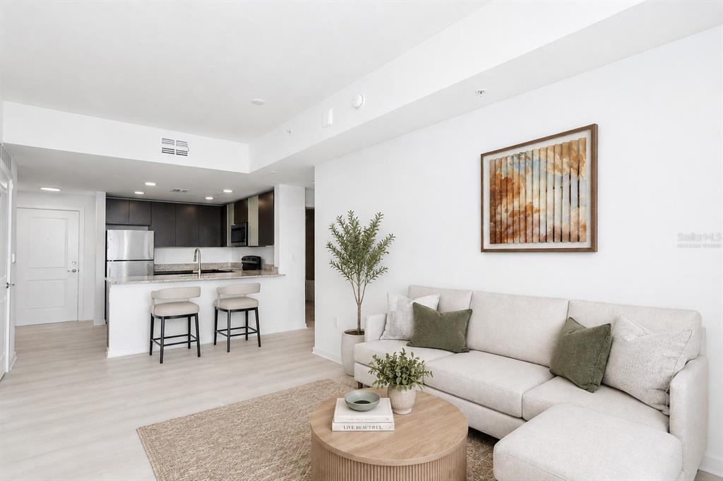 A modern living room with a beige sectional sofa, round coffee table, and open kitchen — 5579 MILLENIA PARK BOULEVARD UNIT 310, ORLANDO, FL