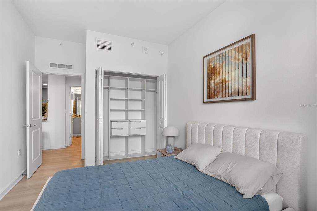 A bedroom features a blue-quilted bed, a white headboard, and an open-shelved closet — 5579 MILLENIA PARK BOULEVARD UNIT 310, ORLANDO, FL