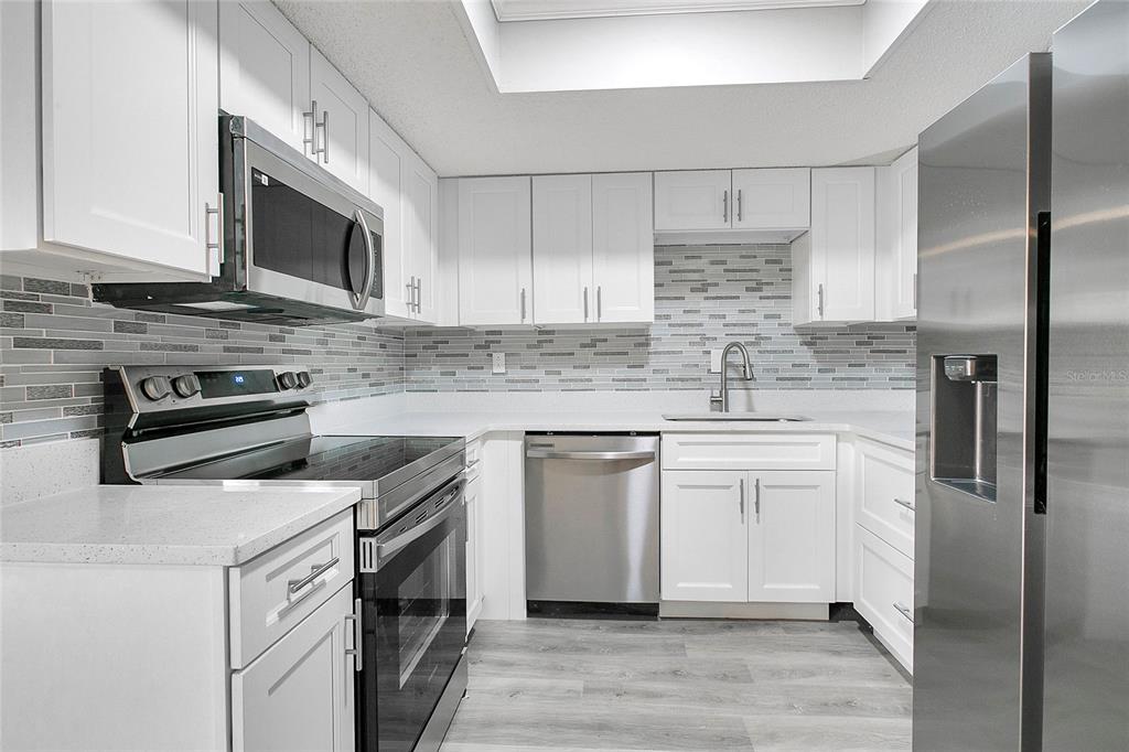 A kitchen features white cabinets, stainless steel appliances, a gray tiled backsplash, and light flooring — 513 FAIRWAYS LANE UNIT B, OCALA, FL
